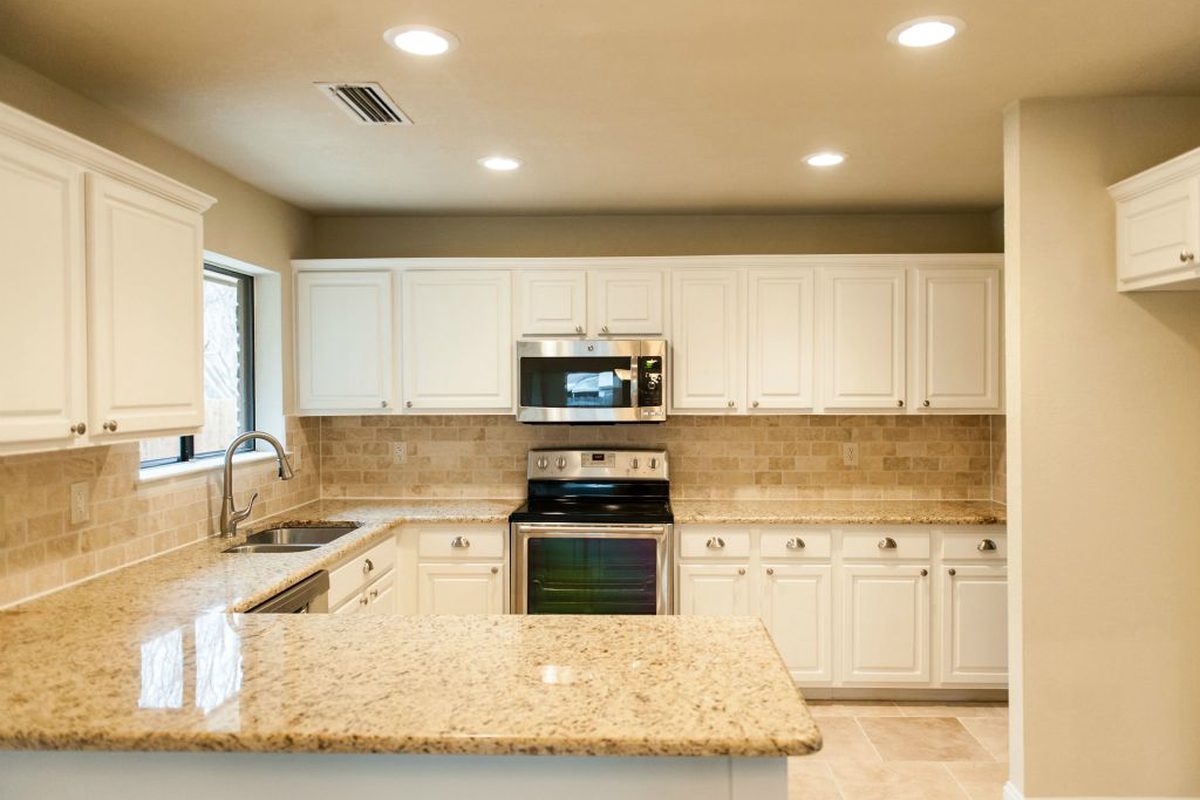 A remodeled kitchen with white cabinetry and granite counters